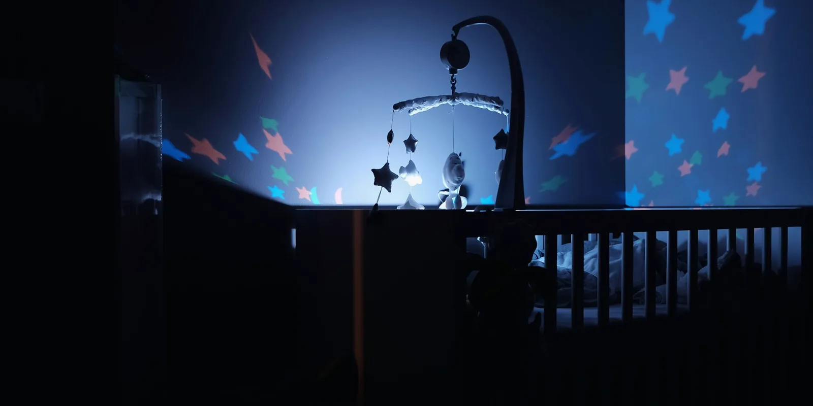 Un mobile de berceau et des étoiles lumineuses dans une chambre d'enfant plongée dans la pénombre