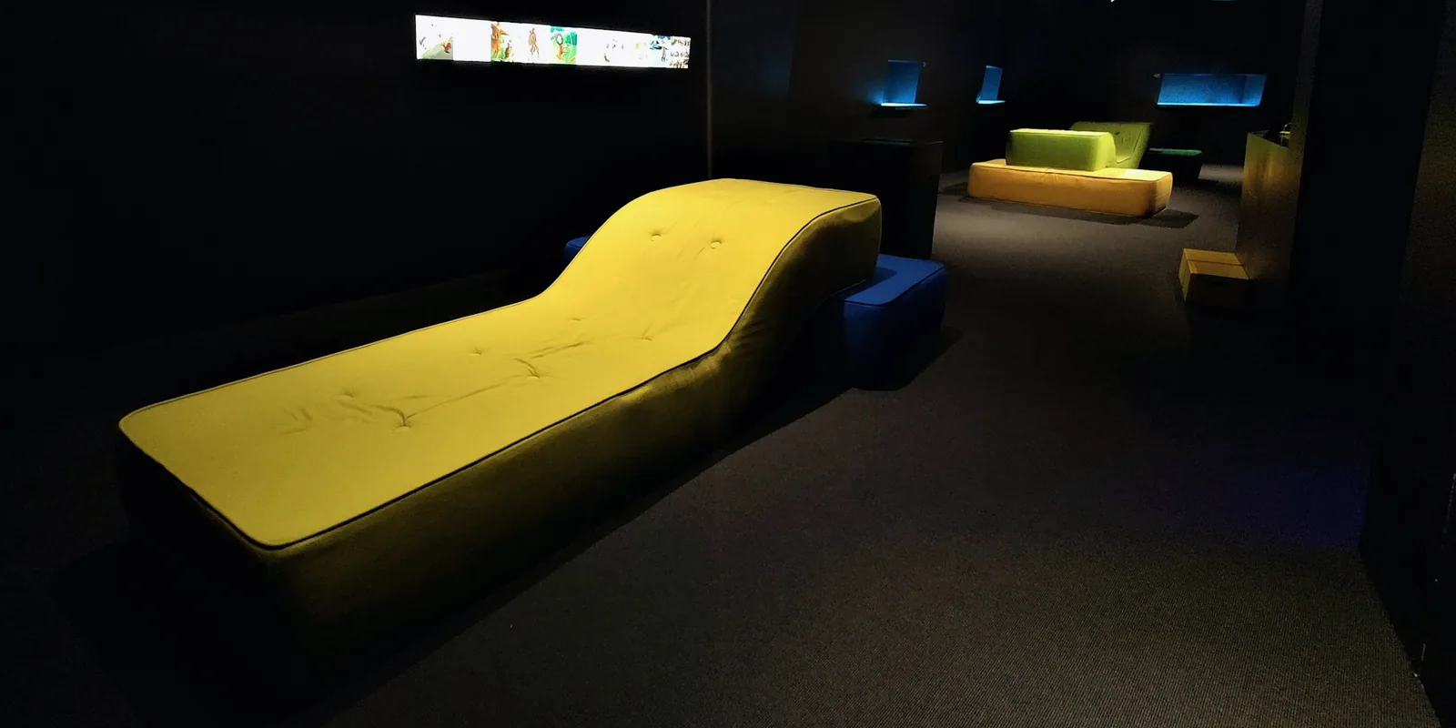 Un salon sombre avec un long canapé jaune et des points de lumière au fond